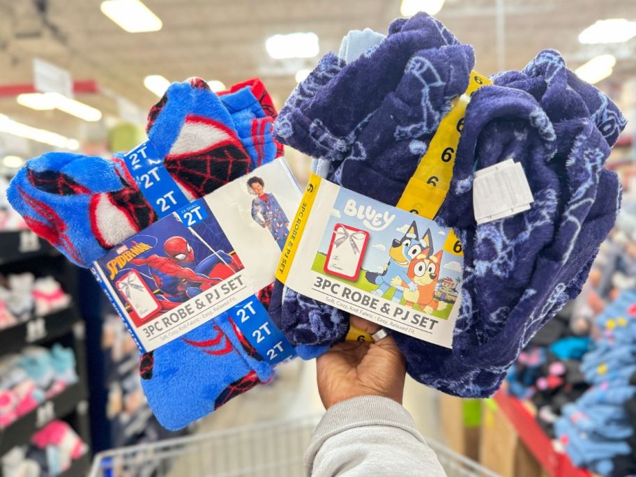 A Hand holding up two boys 23-piece character robe and pajama sets