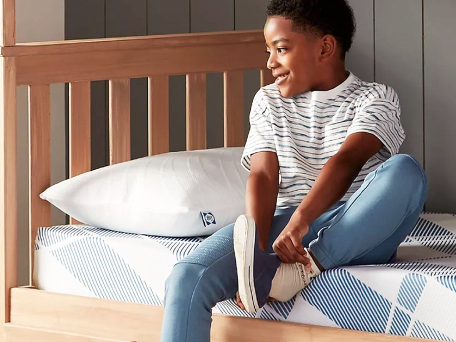 boy sitting on bed putting shoes on