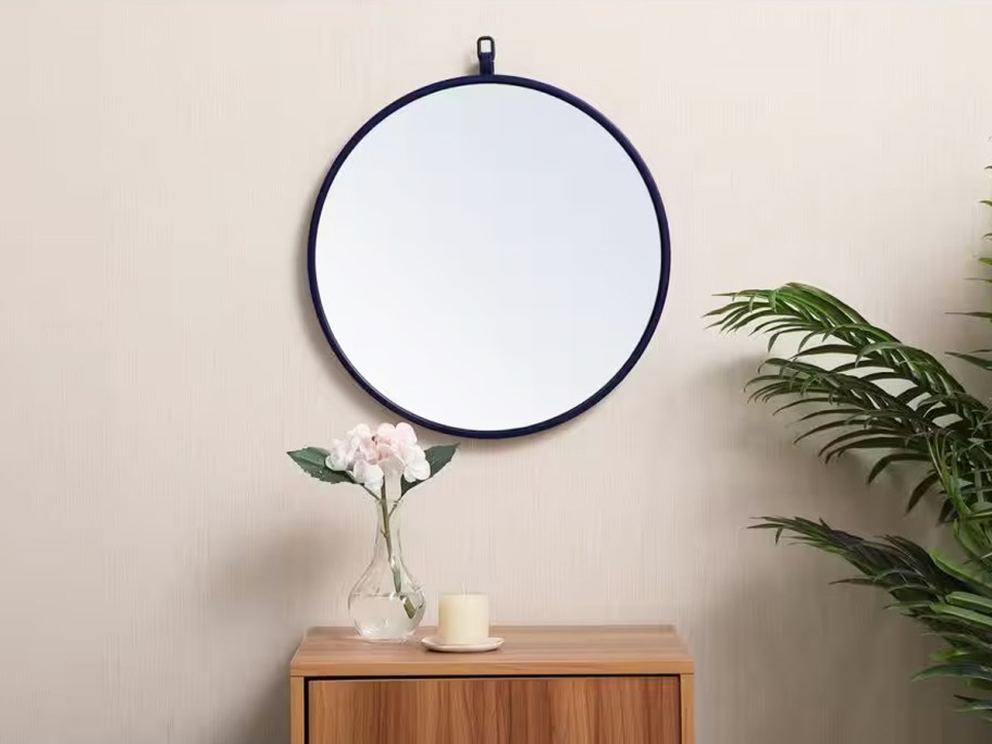 round wall mirror above wood cabinet