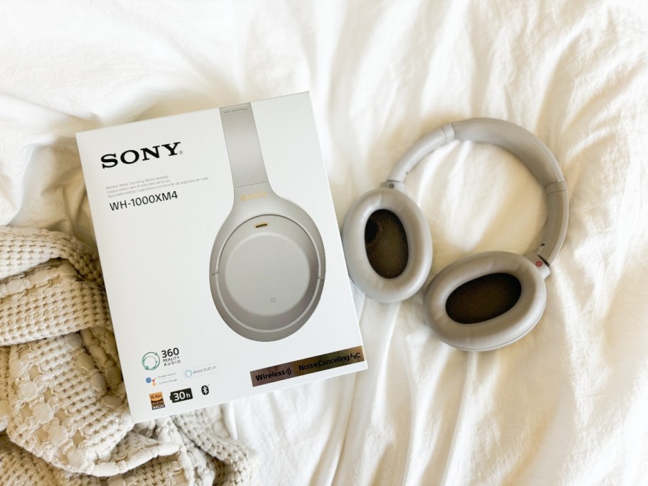 pair of silver Sony headphones on a bed next to the box they onlinee in