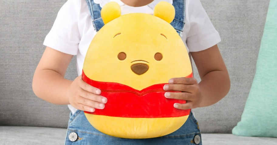 child holding a winnie the pooh squishmallow plush