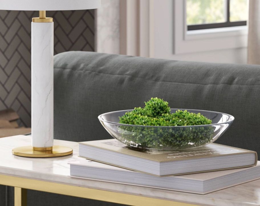 a large round glass bowl filled with greenery sitting on a sofa table