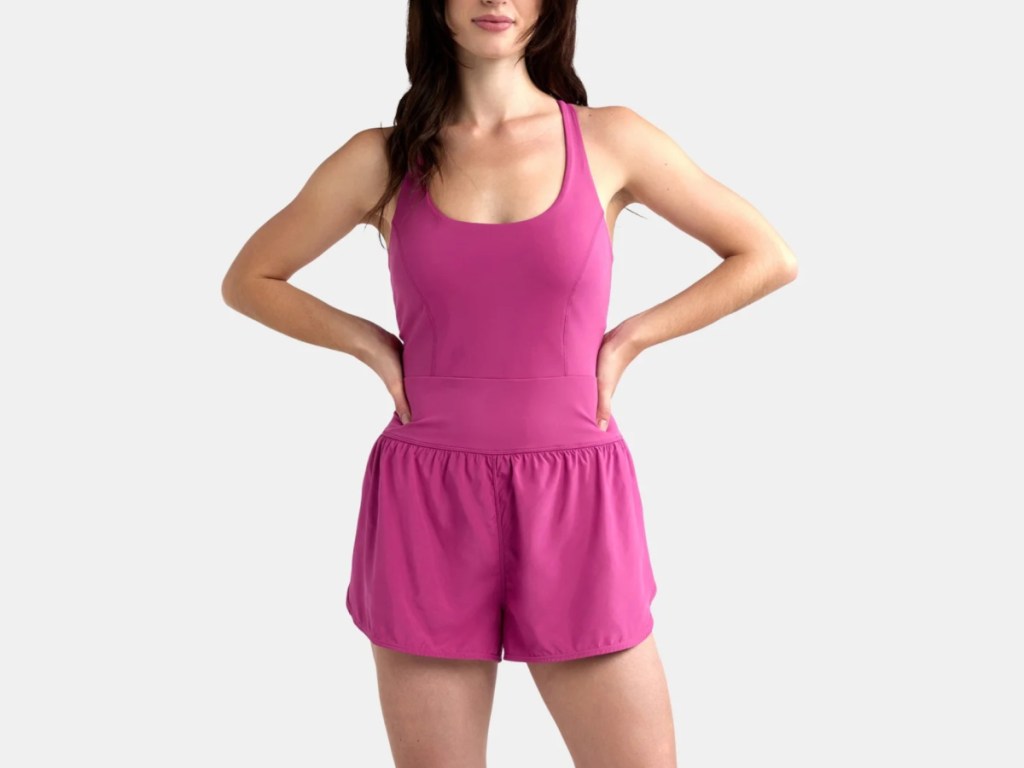 Young woman wearing pink workout romper, and standing with her hands on her hips