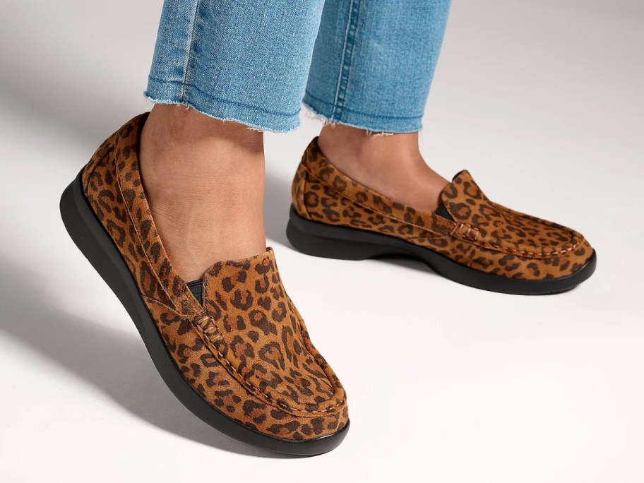 women's feet wearing leopard print slip on shoes with jeans