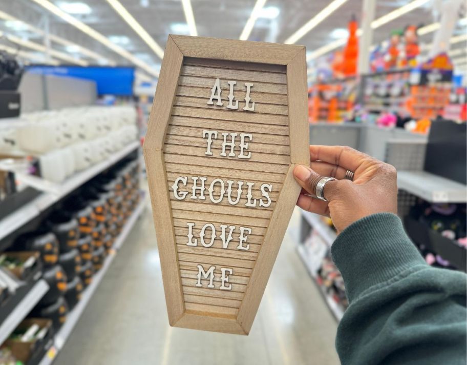 a womans hand holding a coffin-shaped wooden wall decor that says all the ghouls love me