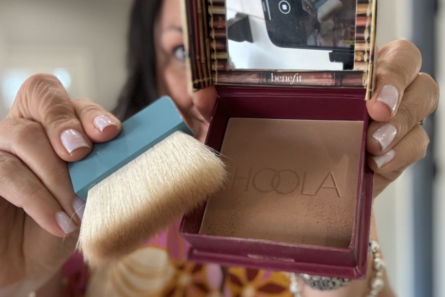 woman holding bronzer and brush in front of face