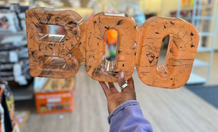 a womans hand holding a boo word shaped divided snack tray