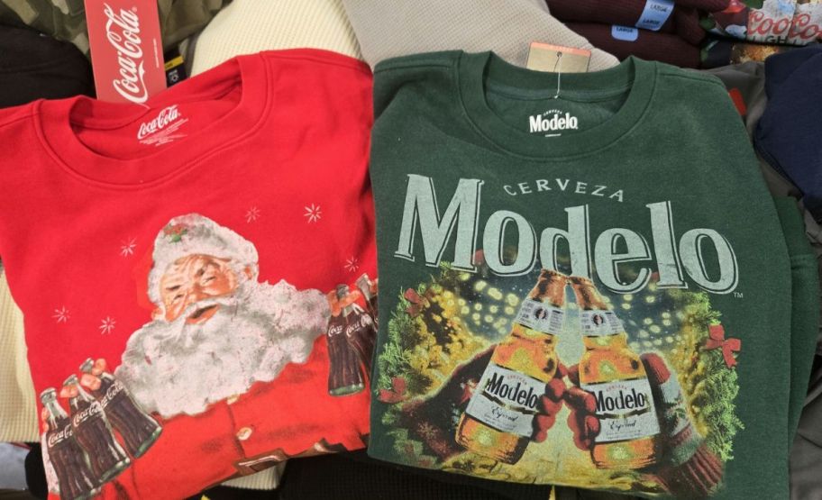 mens coca cola santa and modelo logo holiday sweatshirts on a display table in a store