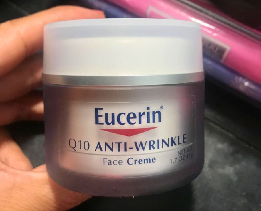 a hand holding a jar of eucerin face cream