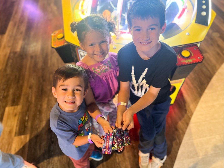 three kids holding arcade game cards in center