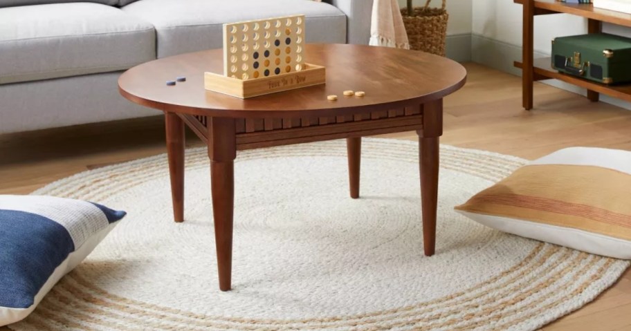 large round cream and tan jute accent rug under a coffee table, throw pillows on the floor, couch behind it