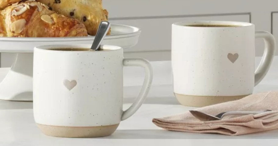 2 white and tan stoneware coffee mugs with tan heart on them on a kitchen island