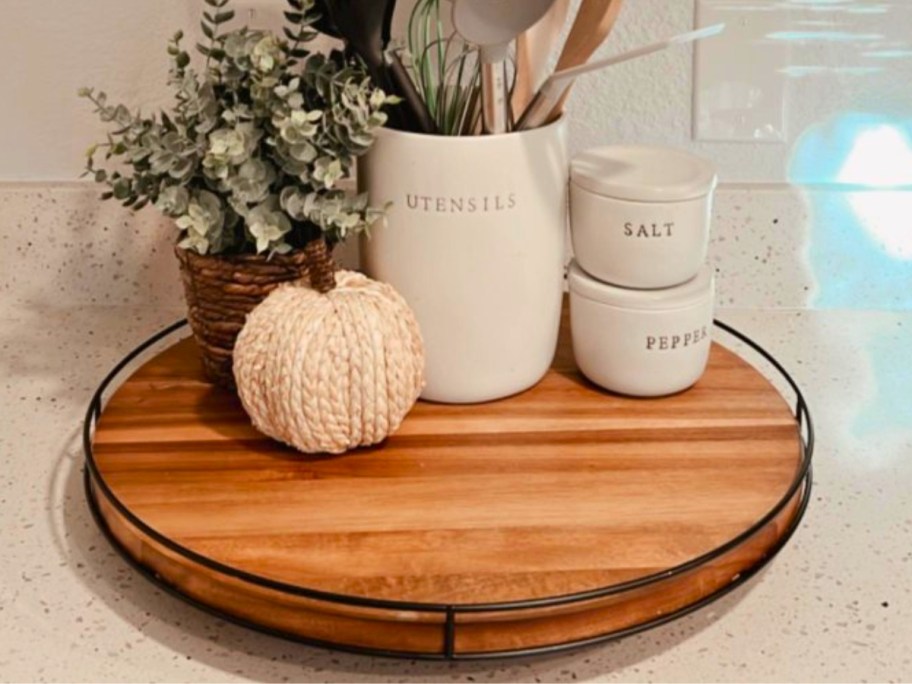 wooden round lazy susan with mini faux pumpkin and plant and white stoneware kitchen tool crock and salt and salt and pepper jars on it