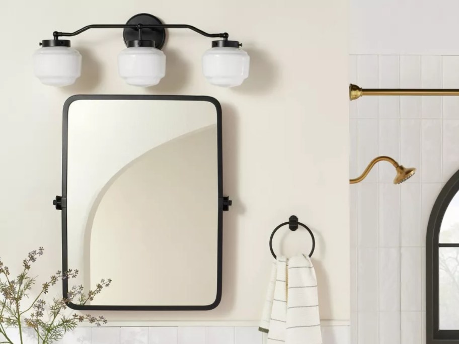 black vanity mirror with a 3 light black and milk glass vanity light above it in a bathroom