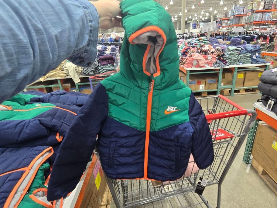 woman hand holding a blue and green kids nike puffer jacket