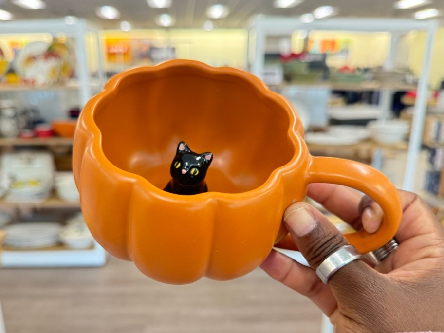 hand holding an orange pumpkin coffee mug that has a black cat inside it