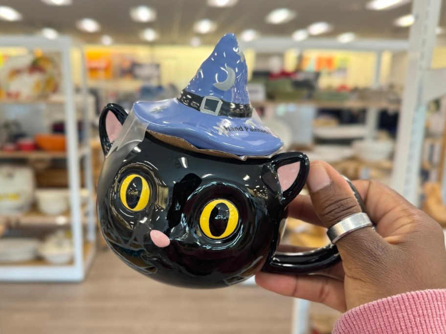 hand holding a Halloween black cat mug with a hat shaped lid