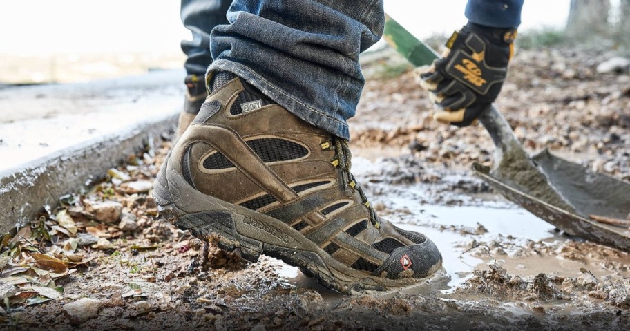 man's feet wearing Merrell work boots in the mud with a shovel working