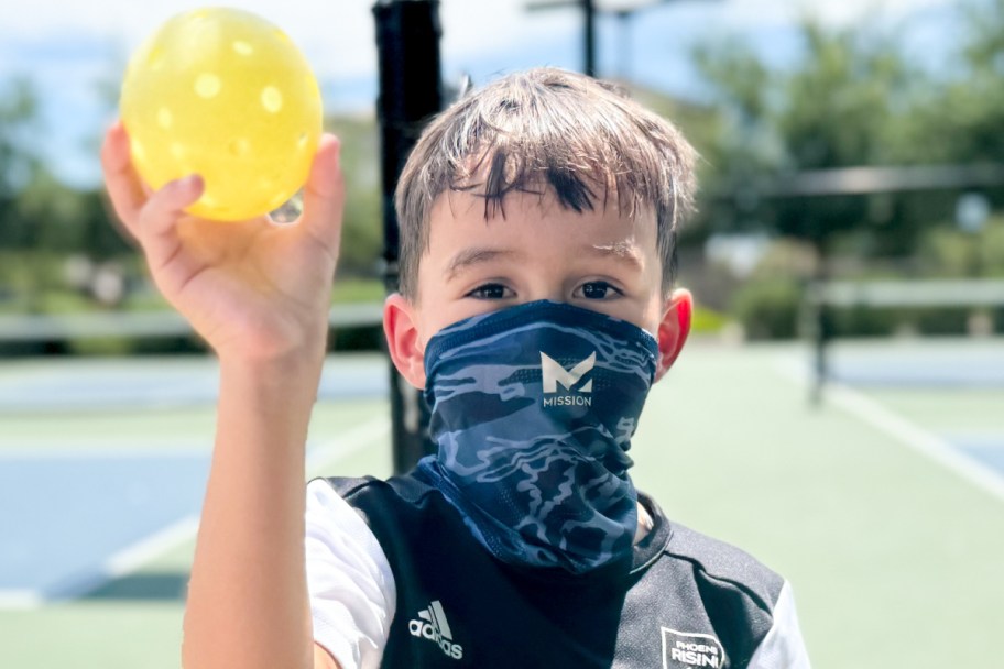 boy holding pickleball wearing face gaiter