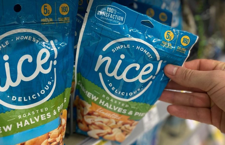 a womans hand grabbing a bag of Nice brand cashews from a store shelf