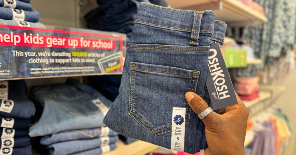 person holding pair of osh kosh jeans in store