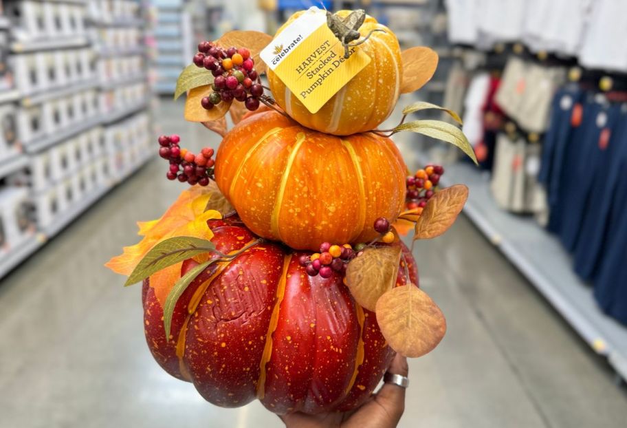 a womans hand holding a pumpkin stack table top decor piece