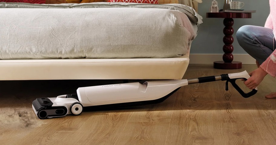 person using white and black vacuum under couch