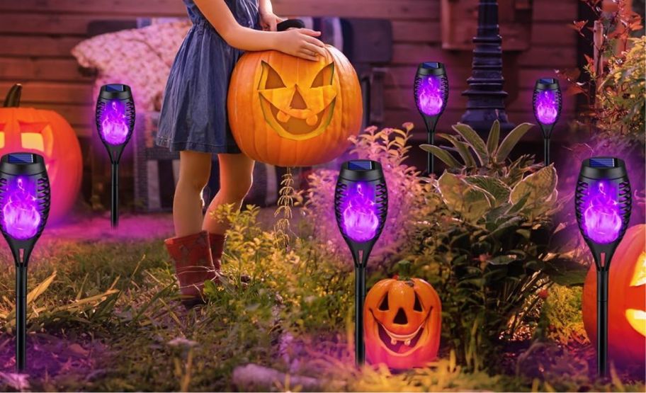 Purple flame solar stake lights with other halloween decor in front of a house