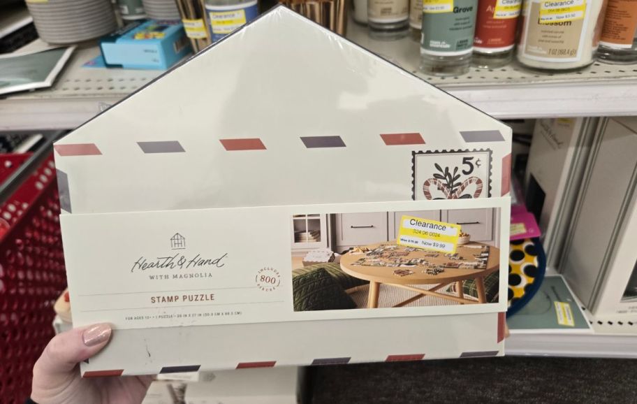 a womans hand holding a wooden stamp puzzle in its packaging.