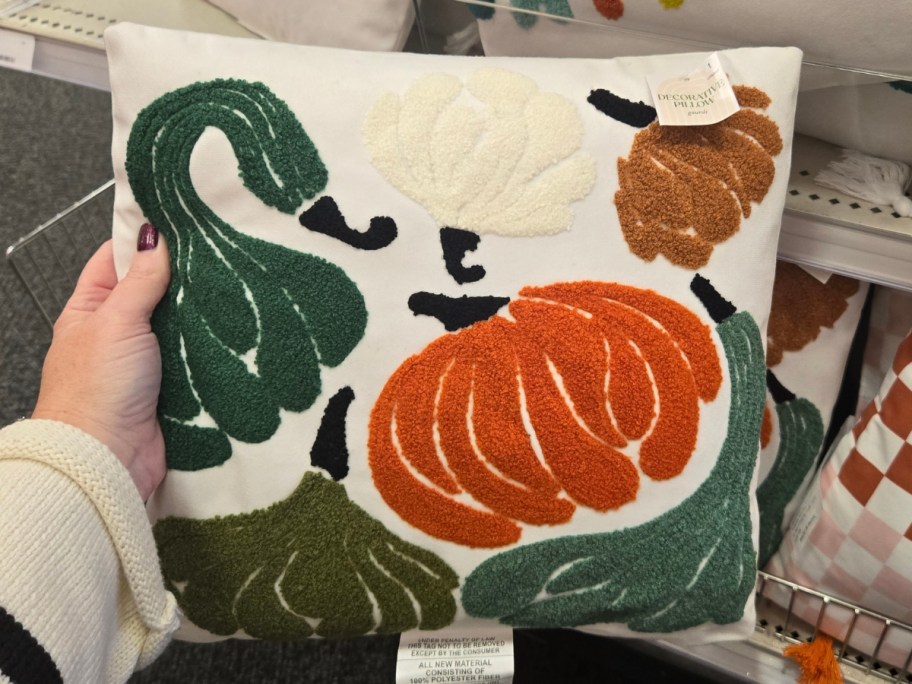 hand holding a white throw pillow that has pumpkins and guards embroidered on it