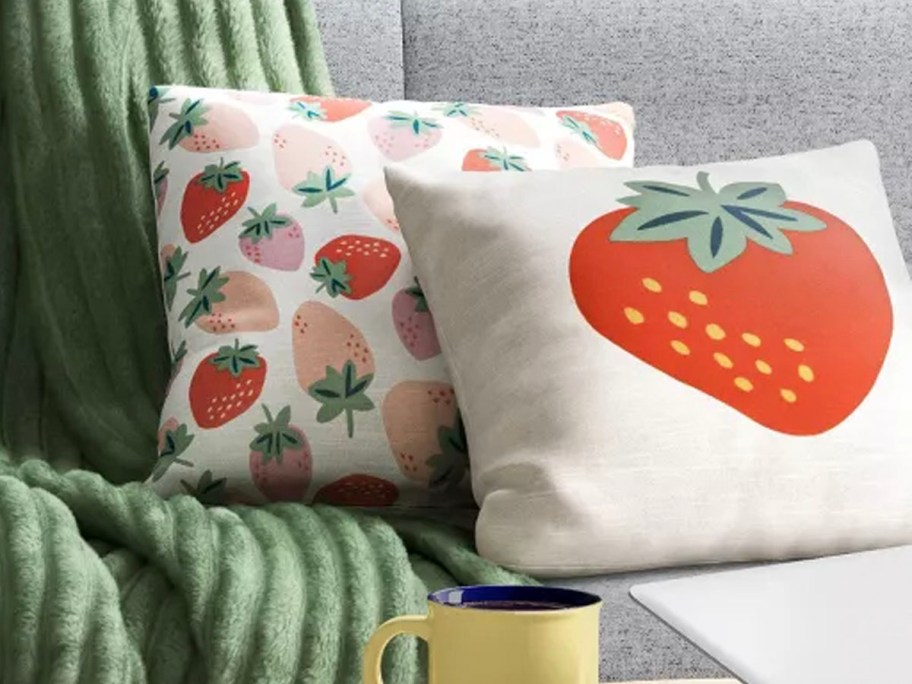 two strawberry throw pillows on couch with green blanket 