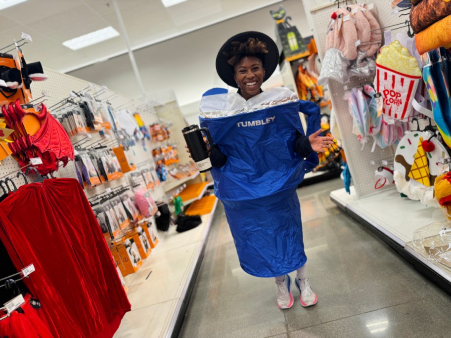 smiling woman wearing a stanley tumbler halloween costume in the middle of a target store aisle