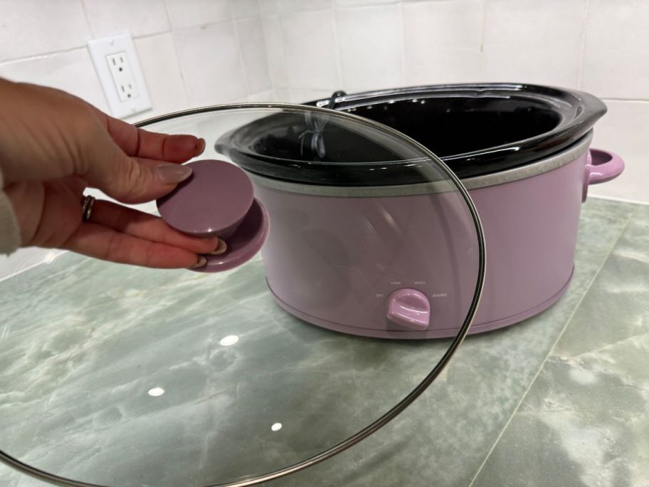 person taking lid off purple slow cooker