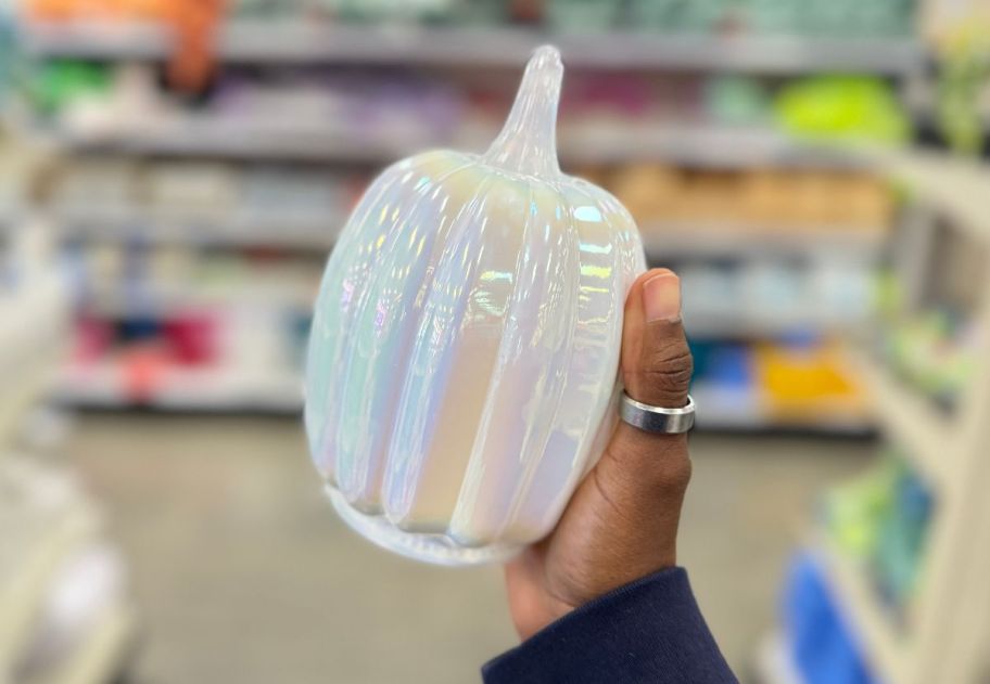 a woman's hand holding a white glass pumpkin