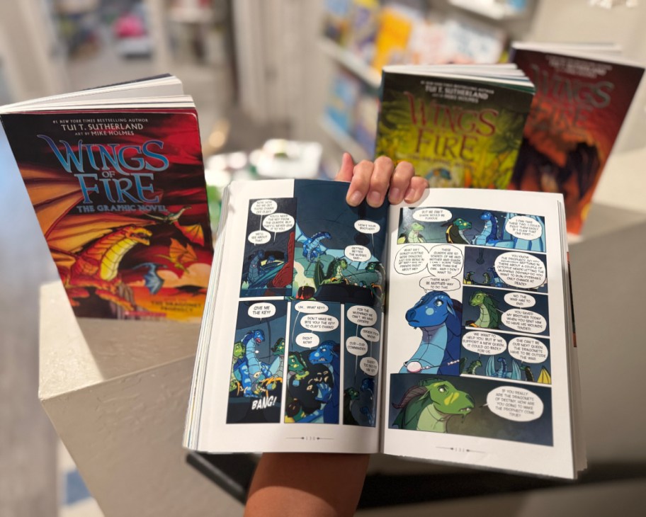 hand holding wings of fire book open next to more books