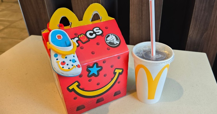 a McDonald's Crocs Happy Meal container with the toy Croc shoe and a small drink in a cup next to it