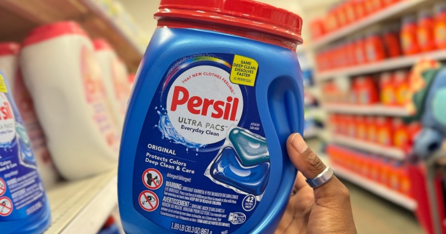 hand holding a large blue and red bottle of Persil Laundry Detergent pacs