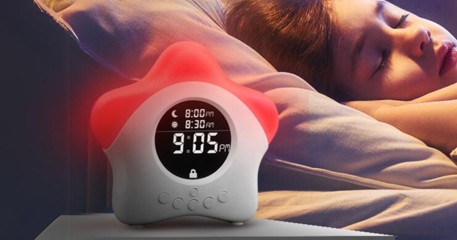 star shaped alarm clock with the top lit up red, little kid sleeping in a bed behind it