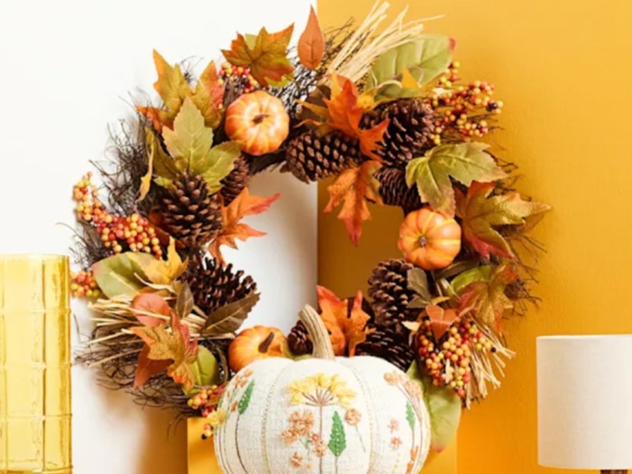 a fall wreath with a decorative floral pumpkin in front of it