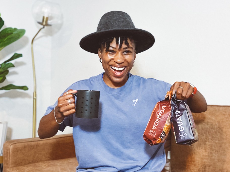 woman holding up black mug and two bags of coffee