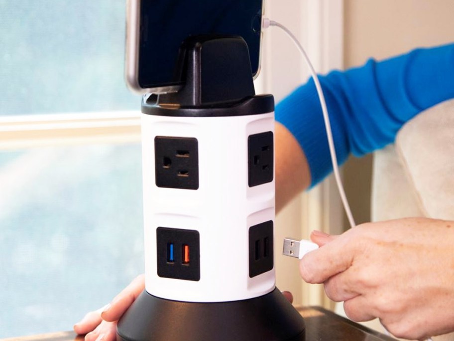 person plugging a phone into a white and black charging tower