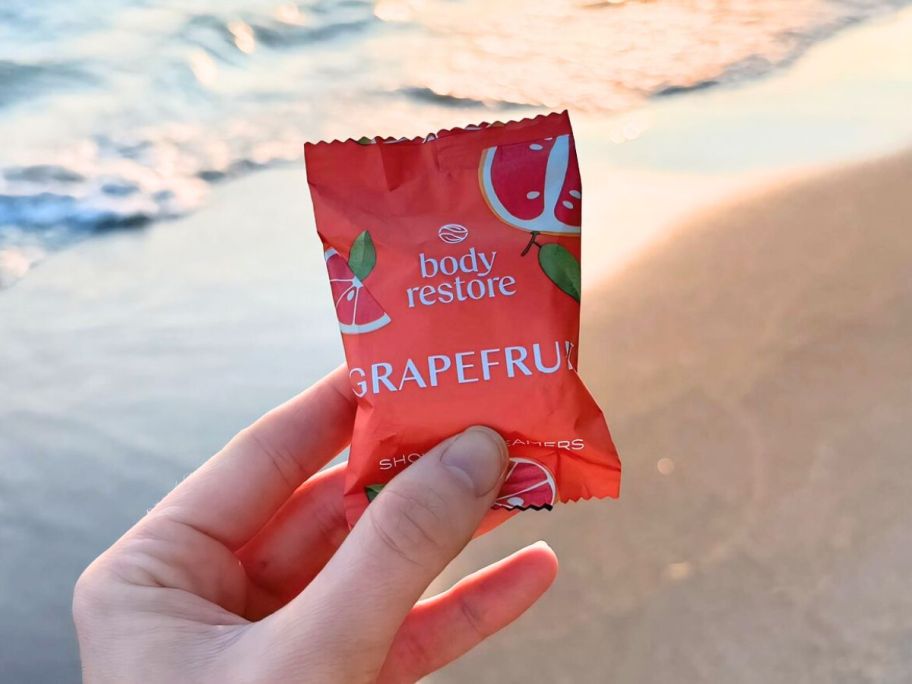 hand holding up a grapefruit body restore shower steamer at the beach