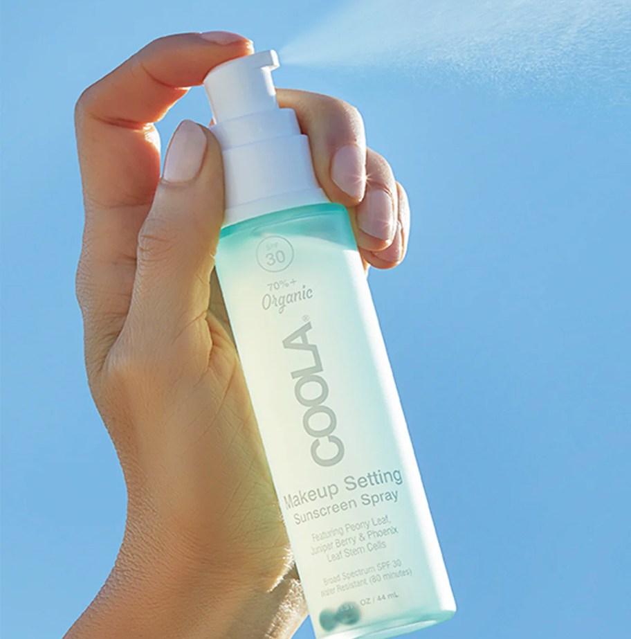 hand spraying a bottle of Coola Makeup Setting Spray