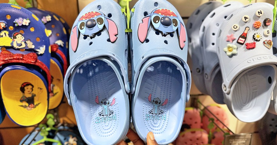 hand touching a pair of blue disney stitch crocs clogs on display