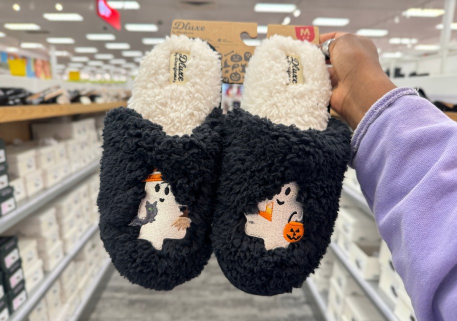 Hand holding up a pair of Halloween slippers from dearfoarm that have ghosts embroidered on the front