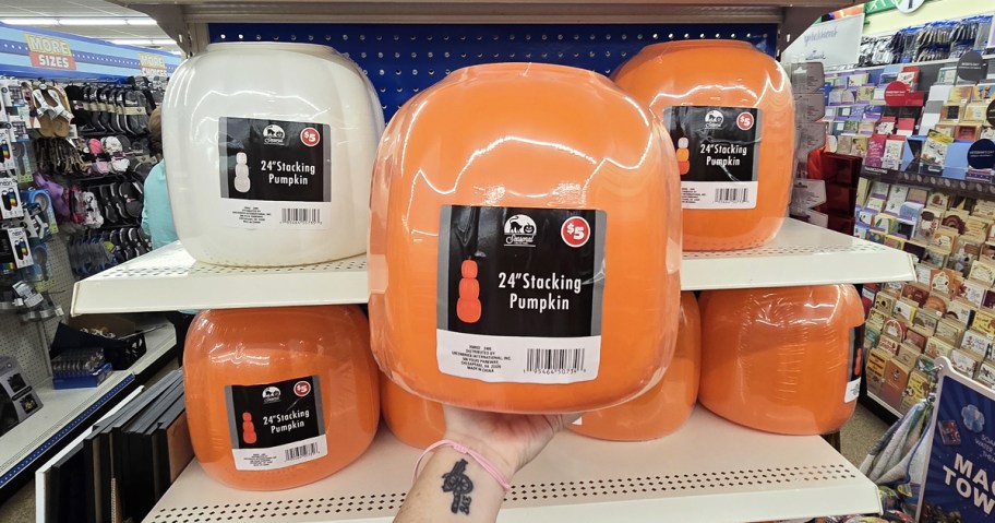 hand holding up an orange stacking pumpkins set in front of shelves filled with more