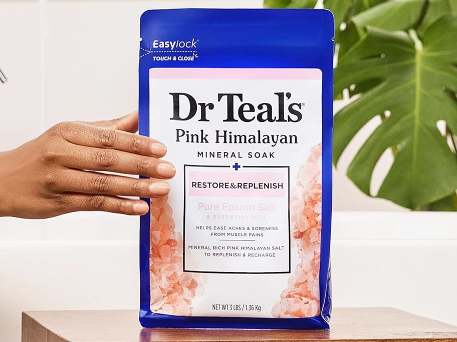 hand grabbing bag of Dr Teal's Pure Pink Himalayan Epsom Salt