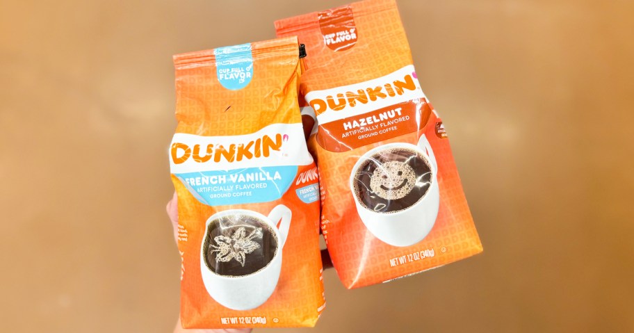 hand holding two orange bags of Dunkin' Ground Coffee