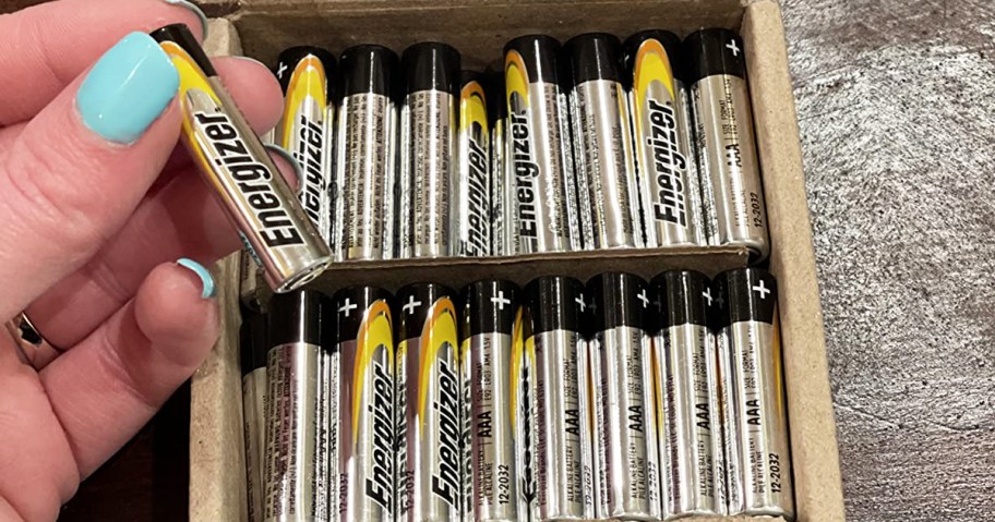 hand holding Energizer AAA Battery in front of box full of batteries