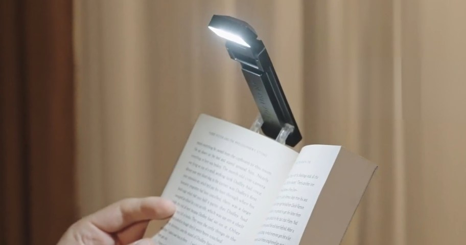 person's hand holding a book with a clip on book light on it